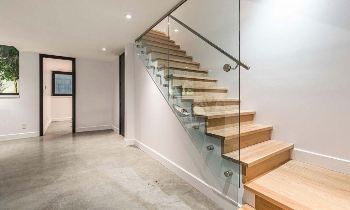 Des escaliers en bois avec une rampe en verre pour offrir une vue sur le sous-sol.