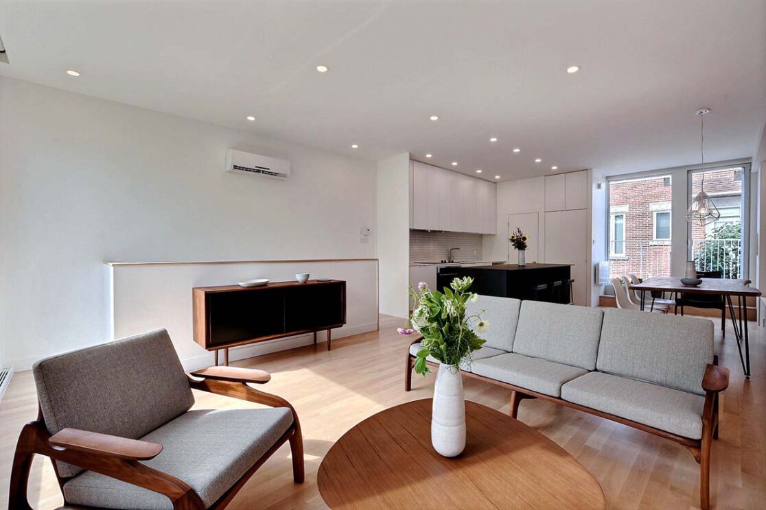 Un salon meublé de canapés gris et de touches de bois, offrant une vue sur la cuisine et la salle à manger.