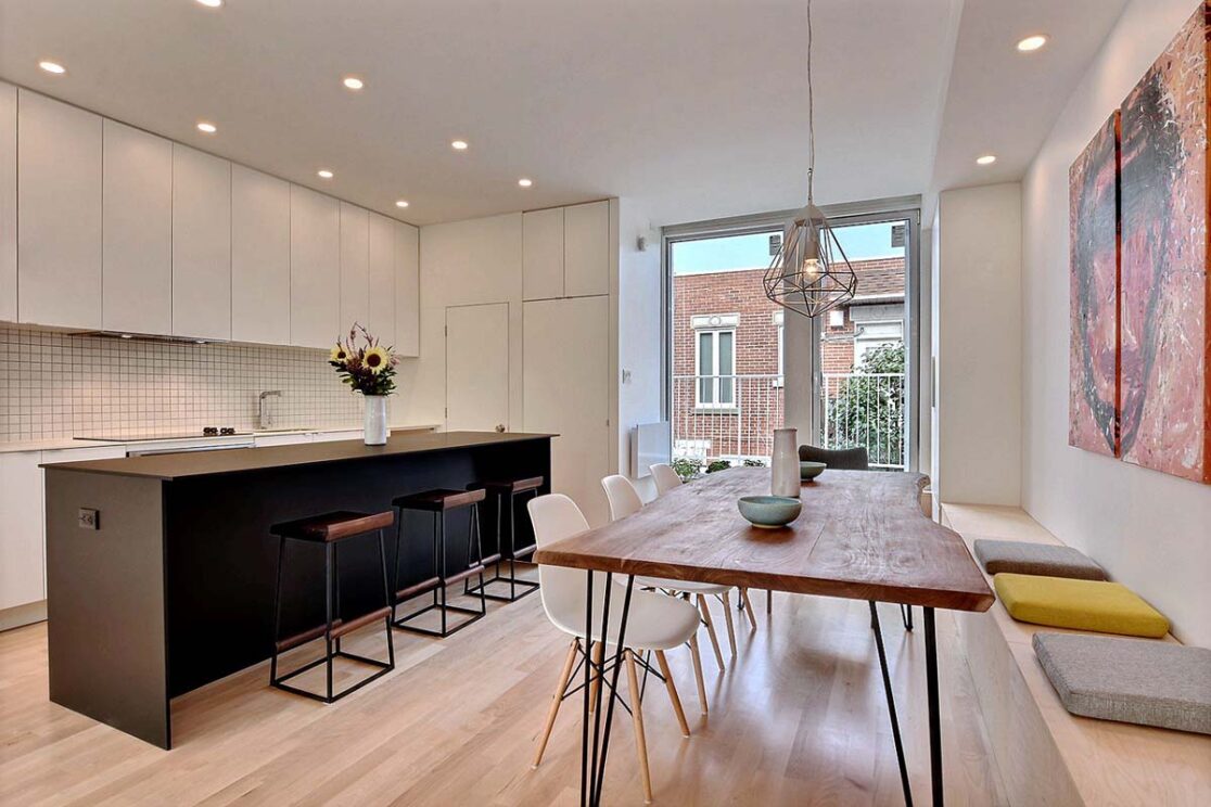 Une cuisine équipée d'armoires blanches et d'un grand îlot brun, accompagnée d'une salle à manger dotée d'une table en bois.