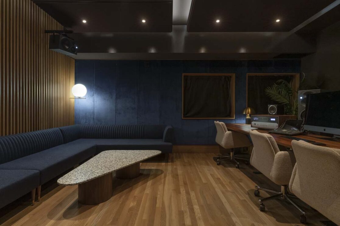 Un studio comprenant un canapé bleu, un mur accentué en velours bleu, ainsi qu'un espace avec des chaises et un ordinateur pour enregistrements.