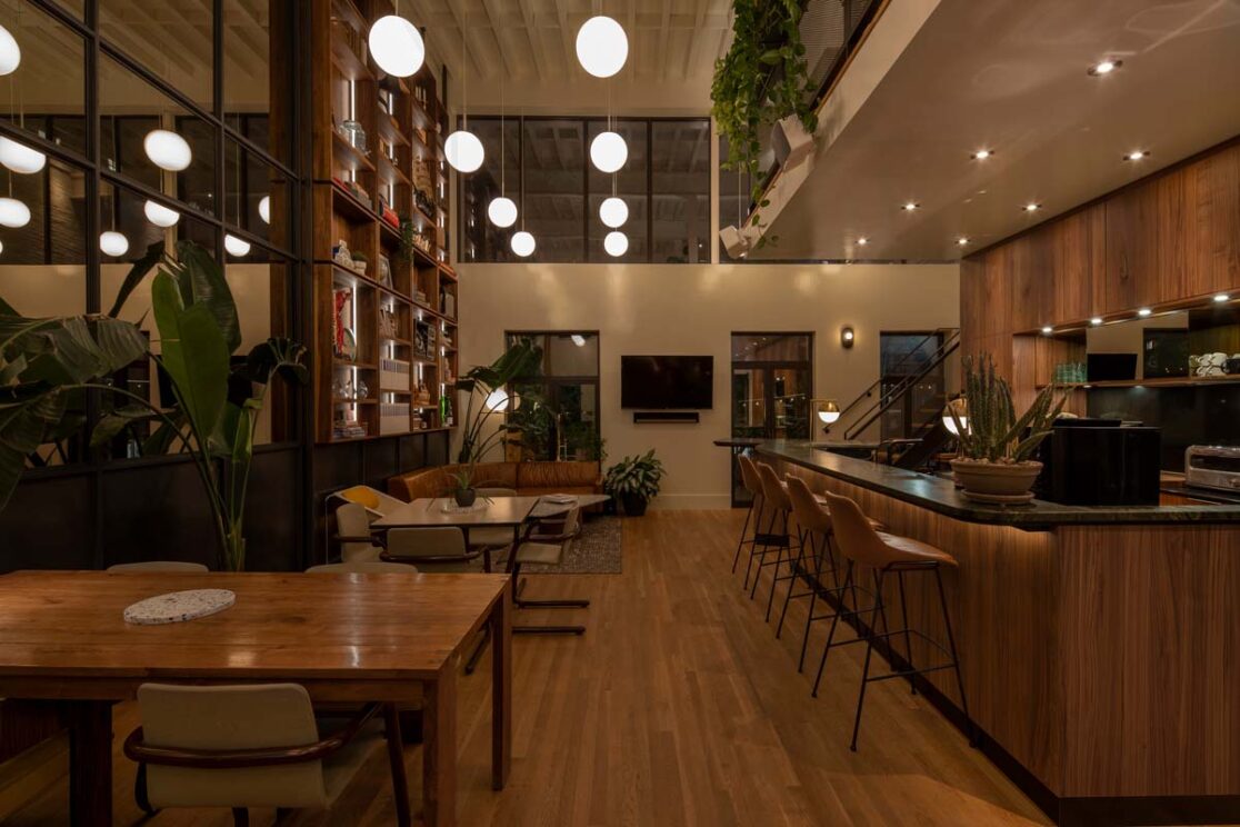 Un bureau spacieux avec une grande bibliothèque, des tables de travail et un grand canapé en soirée.