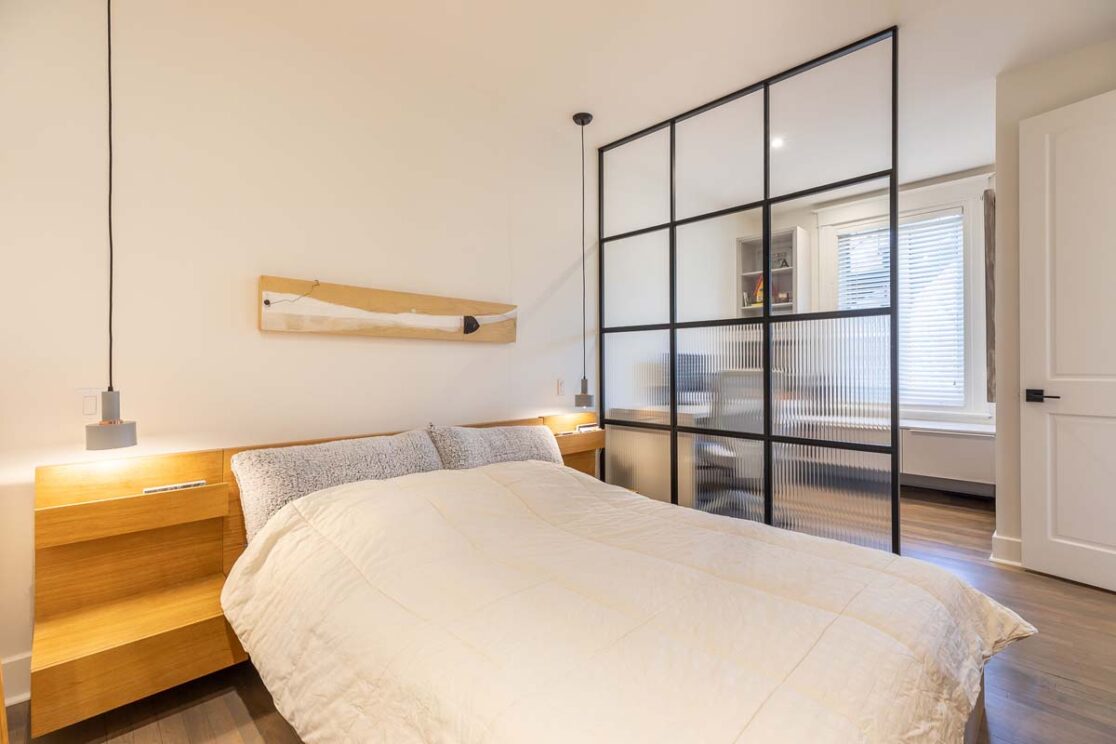 Lit avec séparateur en vitre qui mène vers une section avec un bureau et du rangement.