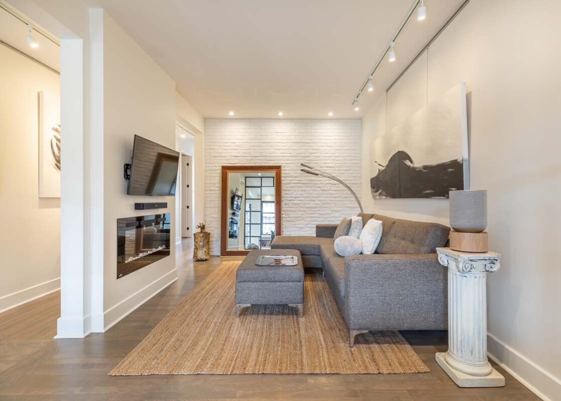 Salon avec un canapé gris, un foyer, un tapis, une télévision et une grande peinture sur le mur.