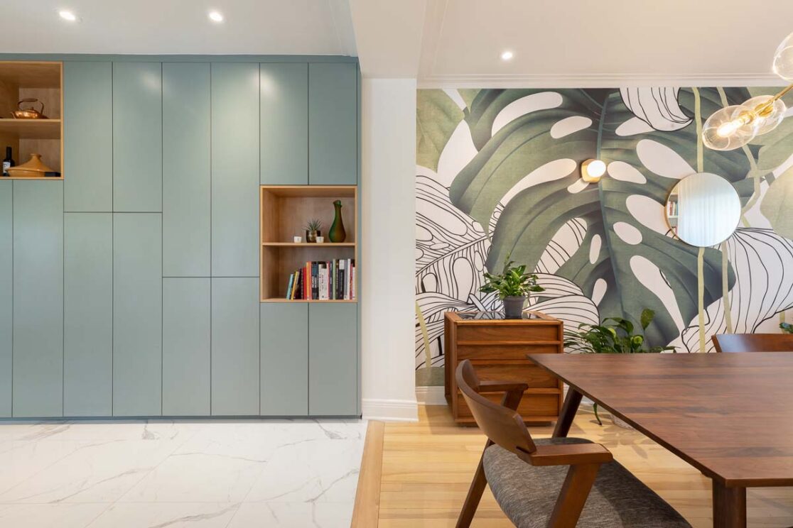 Cuisine et salle à manger avec des armoires turquoise et un joli mur coloré avec des feuillages.