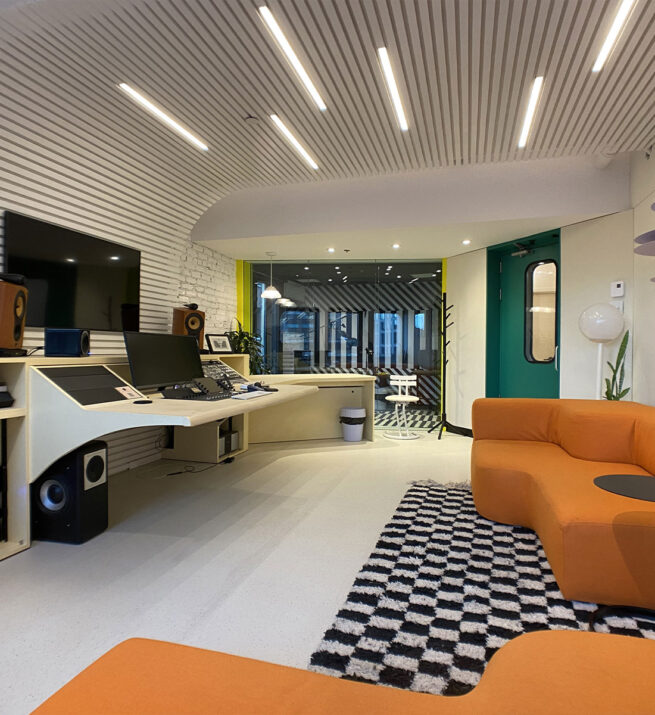 Studio d'enregistrement rétro avec un canapé orange et des équipements d'enregistrement.